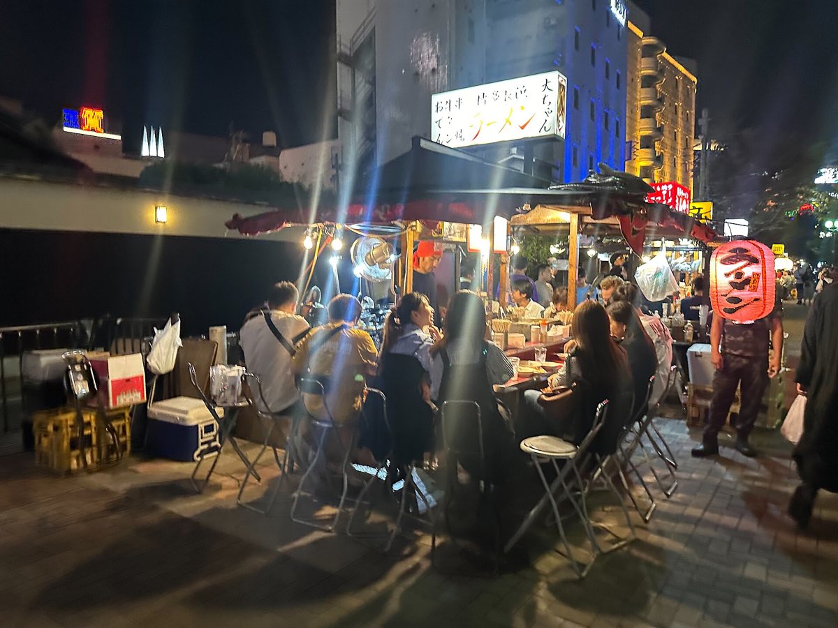 Lit yatai food stalls and their counters on a Hakata street at night